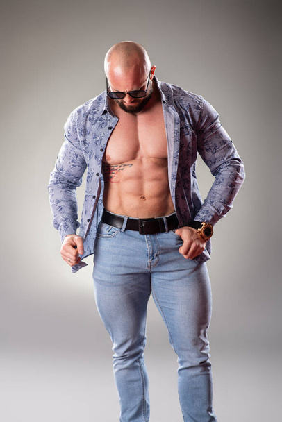 Sexy unbuttoned muscular bodybuider with sunglasses on the gray background - Fotoğraf, Görsel