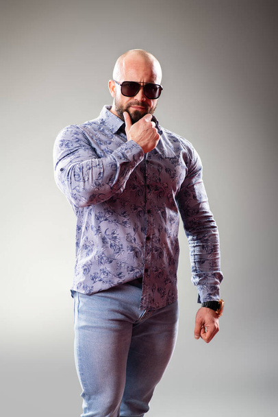 Sexy dressed muscular bodybuider with sunglasses on the gray background - Valokuva, kuva