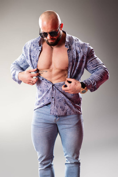 Sexy unbuttoned muscular bodybuider with sunglasses on the gray background - Fotoğraf, Görsel