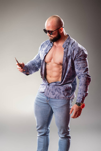 Sexy unbuttoned muscular bodybuider with sunglasses on the gray background. Selfie concept - Valokuva, kuva