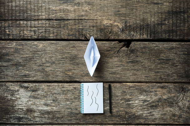 Blocco note con penna e carta fatta origami barca posto su scrivania di legno. Immagine concettuale di visione e ambizione
. - Foto, immagini