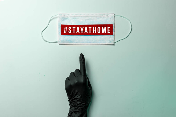 COVID-19, # STAYATHOME. Mão na luva protetora preta, aponta máscara cirúrgica com mostrando a mensagem "# Fique em casa"., Prevenção de vírus e conceito de quarentena global
. - Foto, Imagem