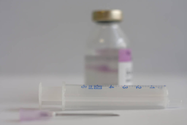 Close-up van de spuit, op de achtergrond injectieflacon met antibiotica, injectiemiddelen gebruikt bij de behandeling van patiënten met longontsteking veroorzaakt door coronavirus covid 19. - Foto, afbeelding