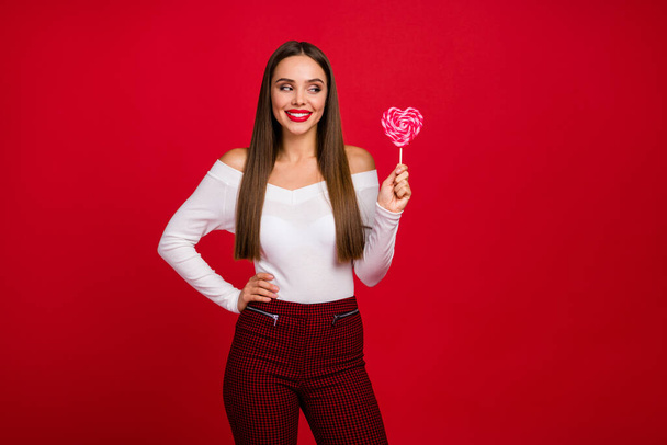 Portrait of positive cheerful girl hold tasty sweet heart shape lolipop look want eat wear classy trend beauty white outfit isolated over bright shine color background - Fotó, kép