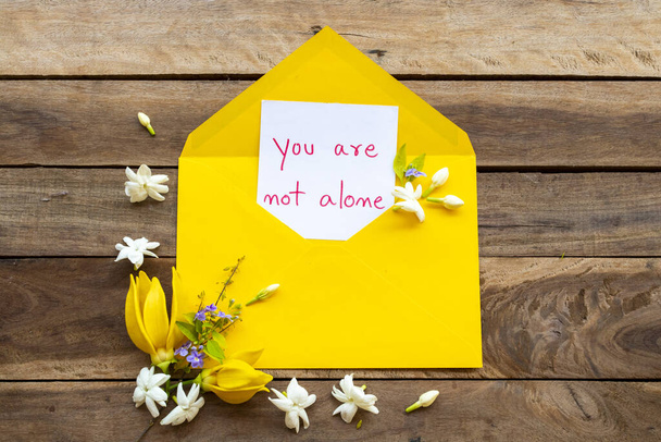 Yalnız değilsin. Sarı zarf içinde sarı çiçekli el yazısı. Yasemin, sarı çiçekler, ylang ylang düzenleme. - Fotoğraf, Görsel