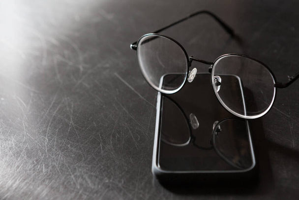 Mise au point sélective des lunettes, smartphone sur fond noir et espace de copie avec lumière et ombre
 - Photo, image
