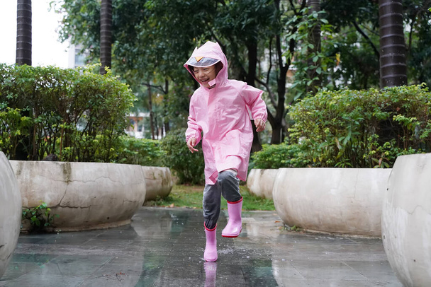 Mała azjatka dziewczyna w różowych butach przeciwdeszczowych i chodzenie podczas sleet jumping w kałuży - Zdjęcie, obraz