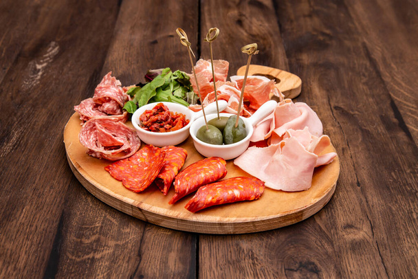Italian antipasto with prosciutto, salami, sun-dried tomatoes, basil and green olives on wooden table. - Fotografie, Obrázek