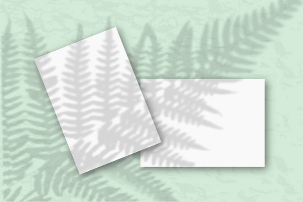 2 fogli di carta bianca contro una parete grigia. Mockup con una sovrapposizione di ombre vegetali. La luce naturale getta ombre dalle foglie di felce. Posa piatta, vista dall'alto
 - Foto, immagini