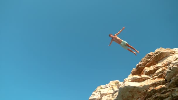 BOTTOM UP: Gioioso uomo caucasico in vacanza estiva immersioni su roccia in una giornata di sole. - Filmati, video