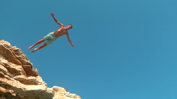BOTTOM UP: Atletische toerist springt van een klif om te duiken in de verfrissende oceaan. - Video