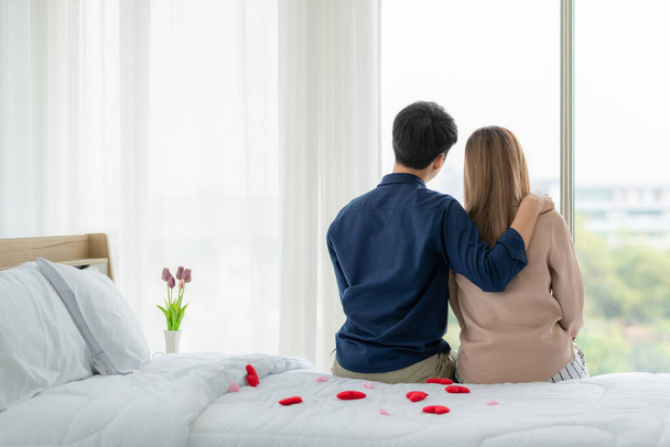 Back angle of young and cute Asian couple sitting together in bedroom with red heart on bed.  Idea for lovers sharing good time together in private moment. Sweet concept for marrying theme. - Fotó, kép