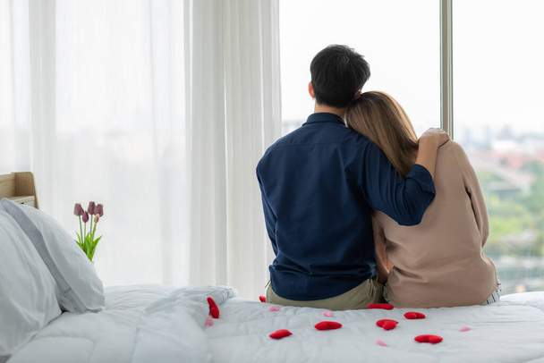 Back angle of young and cute Asian couple sitting together in bedroom with red heart on bed.  Idea for lovers sharing good time together in private moment. Sweet concept for marrying theme. - Foto, immagini