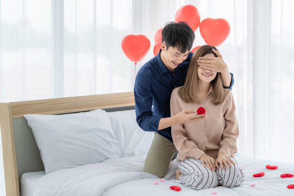 Young and smile face Asian man hug close eyes of young and beautiful pretty woman giving and opening ring box for his lover while she very happy and excited face. Concept for love and ask for wedding - Photo, Image