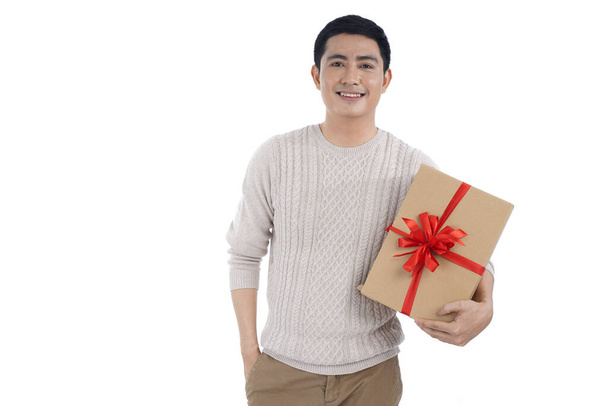 Asian young man in knitted sweater over gray background giving red ribbon gift box - 写真・画像
