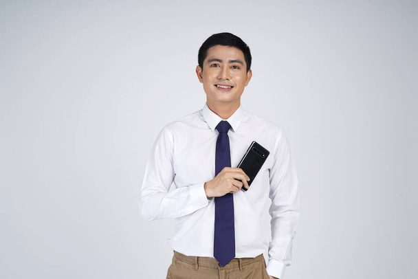 Smiling asian business man standing isolated over gray background, using mobile phone - Valokuva, kuva