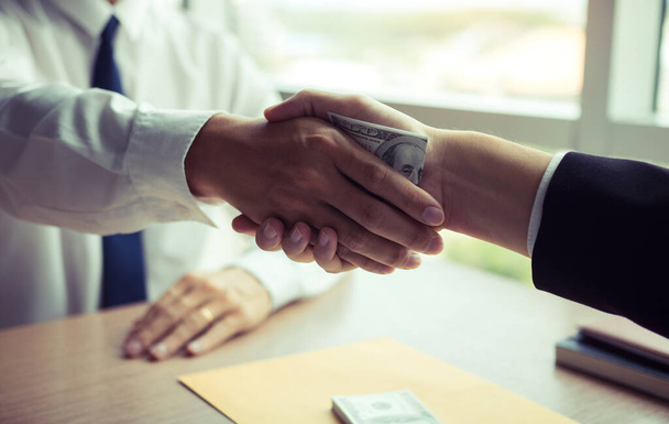 Dos empresarios corporativos estrechando la mano mientras un hombre pone dinero en el documento en la sala de oficina con concepto de corrupción. - Foto, Imagen