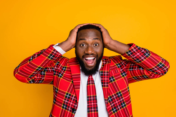 Photo of amazed ecstatic dark skin guy hands on head good mood open mouth listen great news wear plaid red costume blazer white shirt isolated bright yellow color background - Fotografie, Obrázek