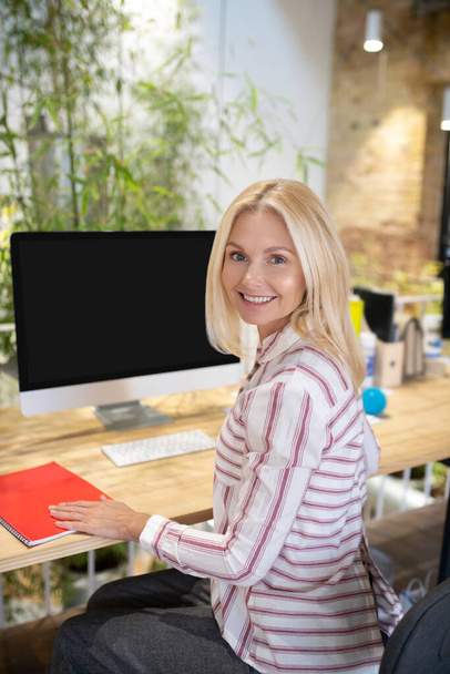 Blonde Frau sitzt am Schreibtisch ihre Hand auf Notizbuch - Foto, Bild