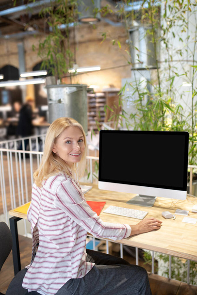 Blonde woman sitting at desk in front of screen, holding mouse - Fotoğraf, Görsel