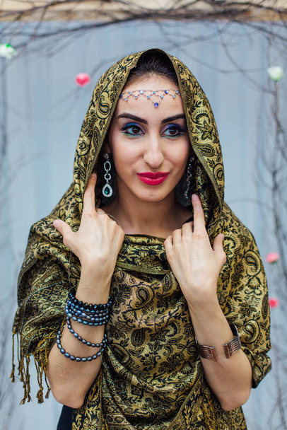 Close up portrait of a beautiful eastern woman with bright makeup and jewelry wearing headscarf. - Фото, зображення