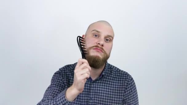 A man with a bald head combing his red beard comb and looking at the camera - Imágenes, Vídeo