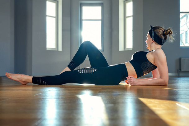 Een vrouw beoefent yoga in een fitnessruimte bij zonsopgang. Concentratie, mooie zonneschijn, stretching, gezonde levensstijl. - Foto, afbeelding