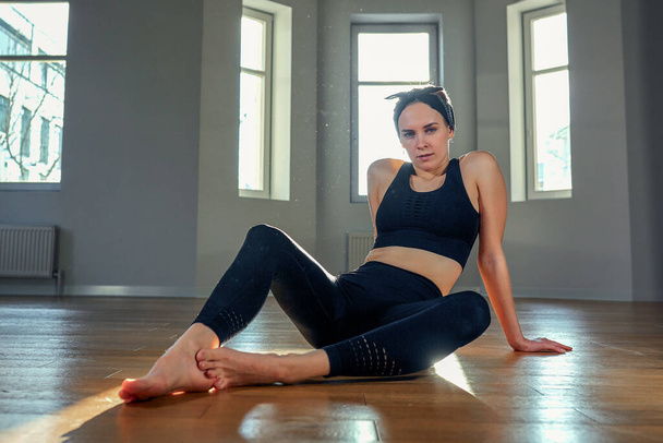 Eine Frau praktiziert Yoga im Morgengrauen in einem Fitnessraum. Konzentration, Sonnenschein, Stretching, gesunder Lebensstil. - Foto, Bild