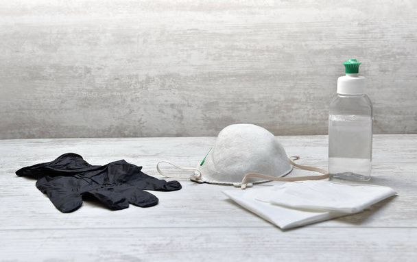 μπουκάλι απολυμαντικό χεριών και μαντήλια δίπλα σε μάσκα σκόνης σε λευκό ξύλινο τραπέζι με γάντι μπλοκ  - Φωτογραφία, εικόνα