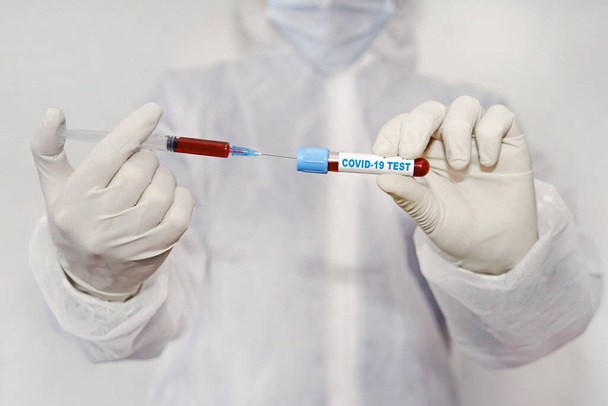 Ένας υπάλληλος εργαστηρίου κρατά μια σύριγγα με ένα εμβόλιο και ένα δοκιμαστικό σωλήνα με αίμα στο χέρι του. έρευνα για το εμβόλιο Coronavirus covid-19. δοκιμαστικό σωλήνα με μολυσμένο αίμα covid 19 - Φωτογραφία, εικόνα