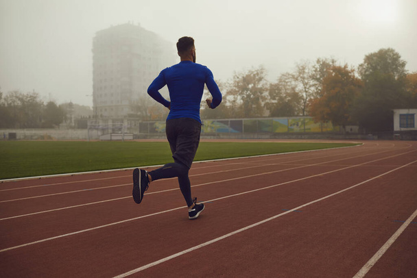 A young athlete runs on a stadium in the fog. - 写真・画像
