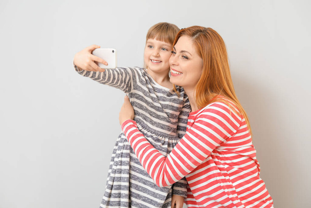 Woman and her little daughter taking selfie on light background - Photo, Image