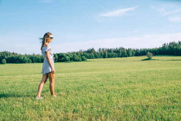 Young woman walking in the green sunny field. Side view - Fotoğraf, Görsel
