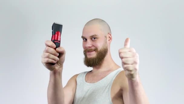 Glatzkopf mit Bart und Clipper in den Händen, der sich rasiert. Daumen hoch - Filmmaterial, Video