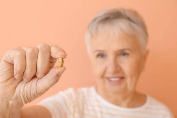 Senior woman with fish oil on color background - Photo, Image