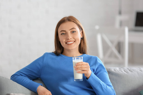 Jonge vrouw in warme trui melk drinken thuis - Foto, afbeelding