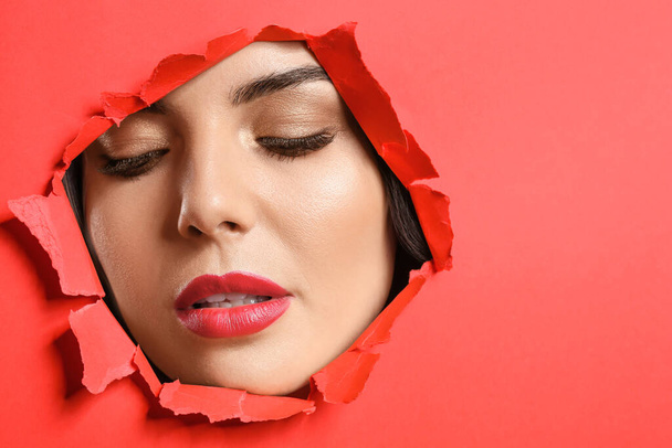 Young woman with beautiful makeup visible through hole in torn color paper - Foto, imagen