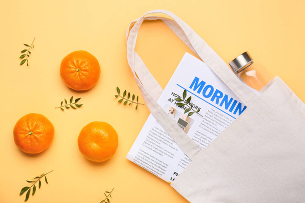 Eco bag with glass bottle, newspaper and orange fruit on color background - Photo, Image