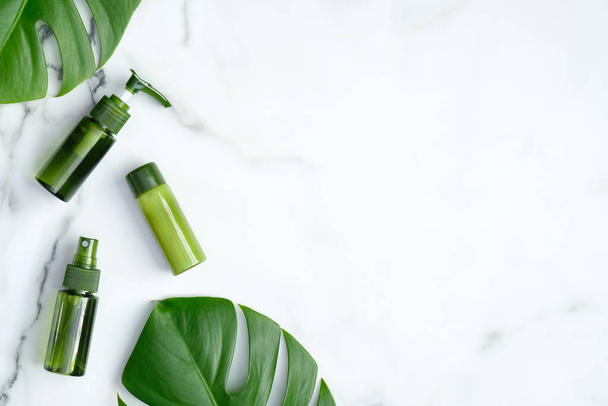 Natürliche Bio-Kosmetikprodukt grüne Flaschen mit Monstera tropischen Pflanzenblättern auf Marmor-Hintergrund. Flache Lage, Draufsicht, Kopierraum. SPA Kosmetikprodukte, Hautpflege und Schönheitsbehandlungskonzept - Foto, Bild