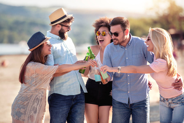 Amici spiaggia festa-celebrazione concetto. Gruppo di amici sorridenti che si accarezzano bottiglie di birra sulla spiaggia. - Foto, immagini