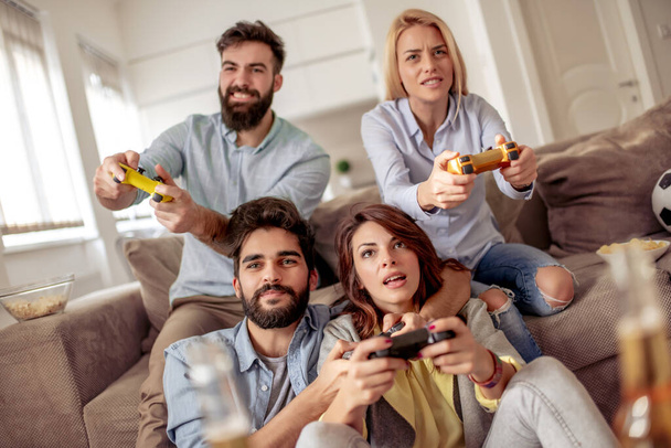 Skupina mladých přátel sedí v moderním bytě a hraje videohry. Přátelství, technologie, hry a domácí koncept. - Fotografie, Obrázek