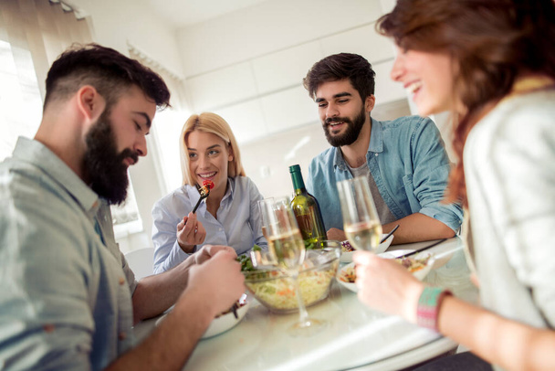 Freizeit, Essen, Essen und Trinken, Menschen und Urlaubskonzept - lächelnde Freunde zu Hause beim Mittagessen und Wein trinken. - Foto, Bild