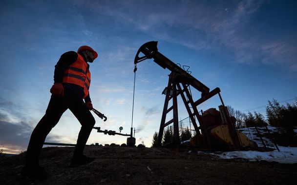 Matala kulma mies öljy työntekijä seisoo lähellä öljypumppu jack alla kaunis ilta taivas
 - Valokuva, kuva