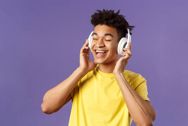 Close-up portret van zorgeloze, jonge vrolijke man met dreads, ogen dicht en glimlachend blij als het luisteren naar geweldige nieuwe lied favoriete artiest geüploade muziek platform, draag een koptelefoon - Foto, afbeelding