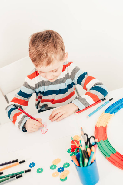 Child drawing picture of mom while sitting at white desk - Foto, Bild