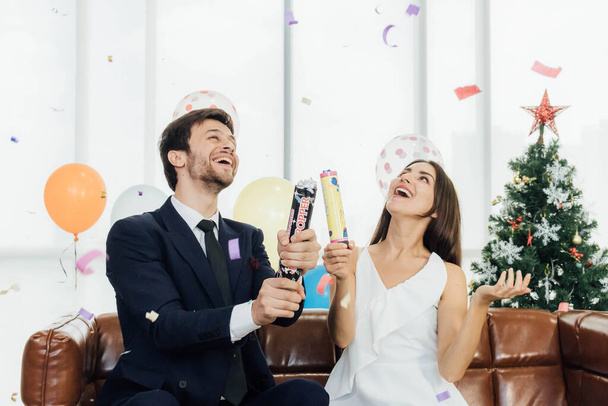 Young and attractive couple celebrate Christmas and new year with confetti poppers. - Photo, Image
