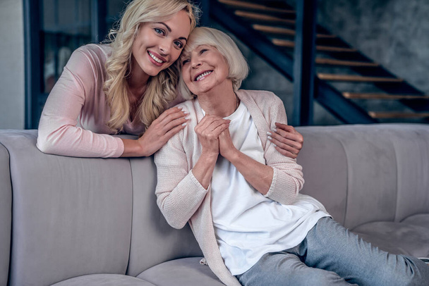 Senior woman and her attractive daughter spending time together at home and sitting on sofa. Happy Mothers' Day - Foto, Imagen