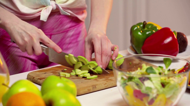 Rajatut näkymä nainen leikkaus avokado lähellä hedelmiä ja salaattia pöydällä
  - Materiaali, video