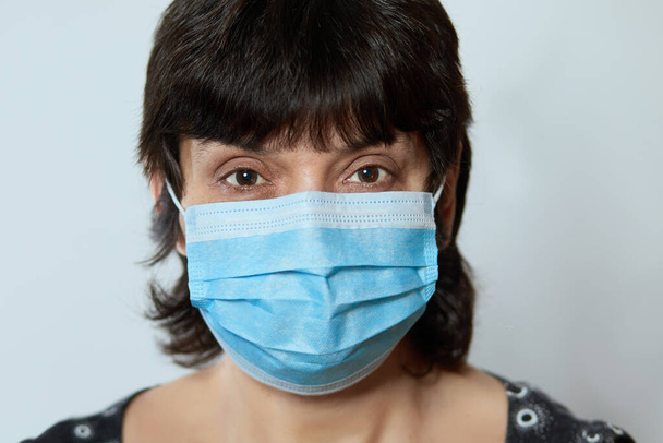 Yüz maskesi takan genç bir kadının portresi, kameraya bakıyor, yakın plan, gri arka plan izole edilmiş. Grip salgını, koronavirüs, toz alerjisi, virüse karşı koruma. Şehir hava kirliliği kavramı  - Fotoğraf, Görsel
