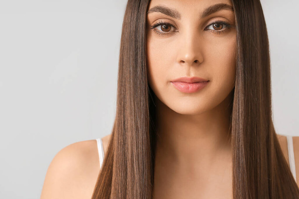 Nuori nainen, jolla on kauniit suorat hiukset harmaalla taustalla
 - Valokuva, kuva